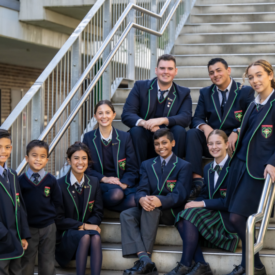 A group of high school students sitting on the steps at their Catholic school.
