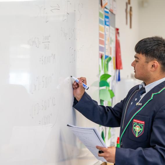 A high school student doing some complex mathematics on a white board.
