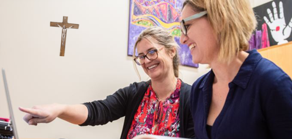 Two females teachers looking at laptop in staffroom