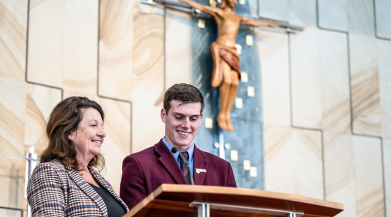 A student and a teacher standing in front of a lectern in a church.