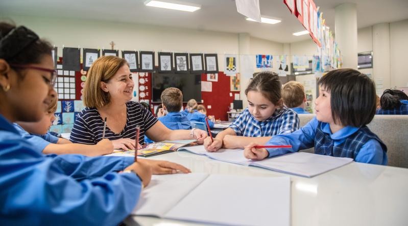 A teacher at a table with some students teaching them writing.